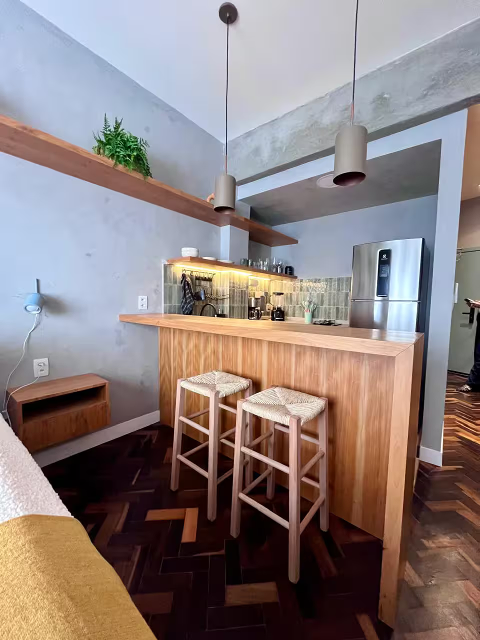 Detalhe da cozinha integrada em loft em Copacabana, mostrando a bancada em madeira clara com banquetas e armários planejados.